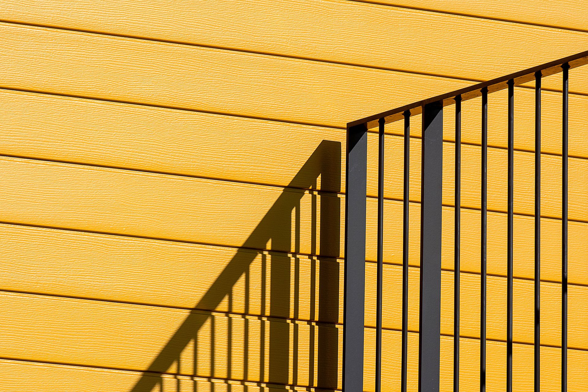 Artistic capture of shadow cast by metal railing on a vibrant yellow wall.
