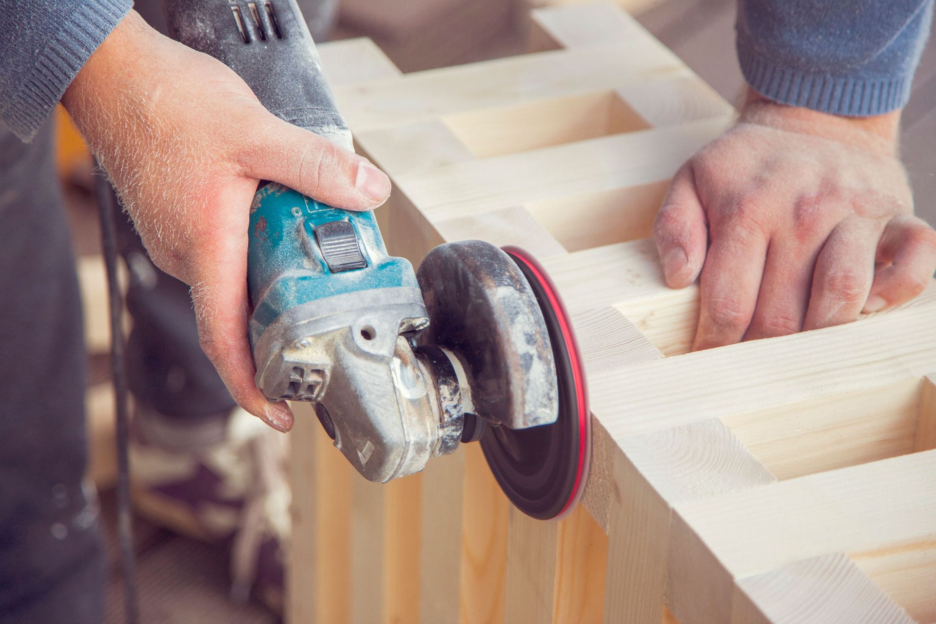 Crop unrecognizable male carpenter using angle grinder to polish wooden construction in light joinery